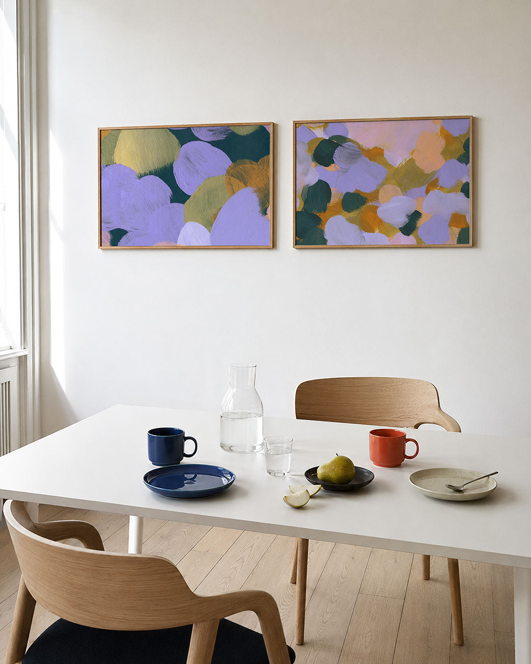 Twee liggende posters met ovale kleurvlakken in lila, groen en oranje, aan de muur in een interieur