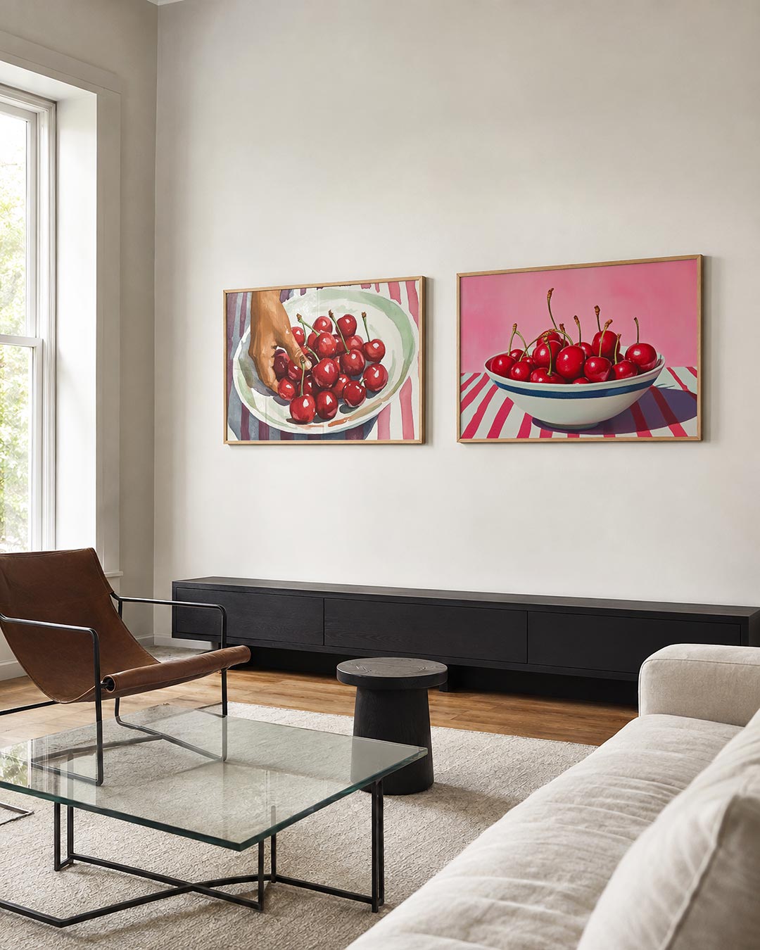 Twee liggende posters met een hand die naar rode kersen op een wit bord reikt, aan de muur in een interieur