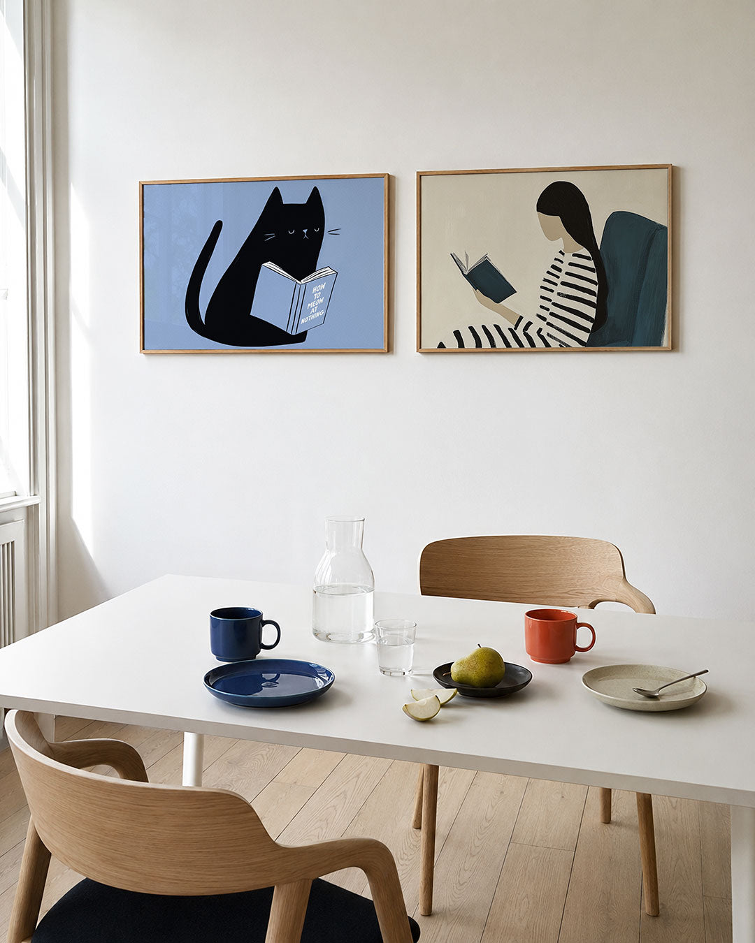 Twee liggende posters met een zwarte kat met een boek op een zachte blauwe achtergrond, aan de muur in een interieur